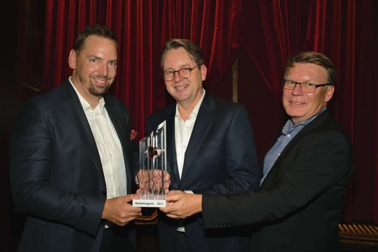 Drei Männer im Anzug halten Marketingpreis Pokal in der Hand