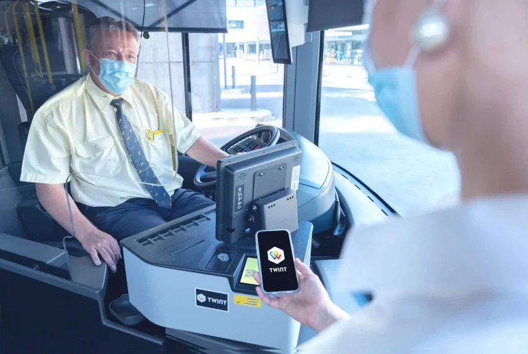 Postautochauffeur schaut auf Gast der mit Smartphone in der Hand mit TWINT bezahlt