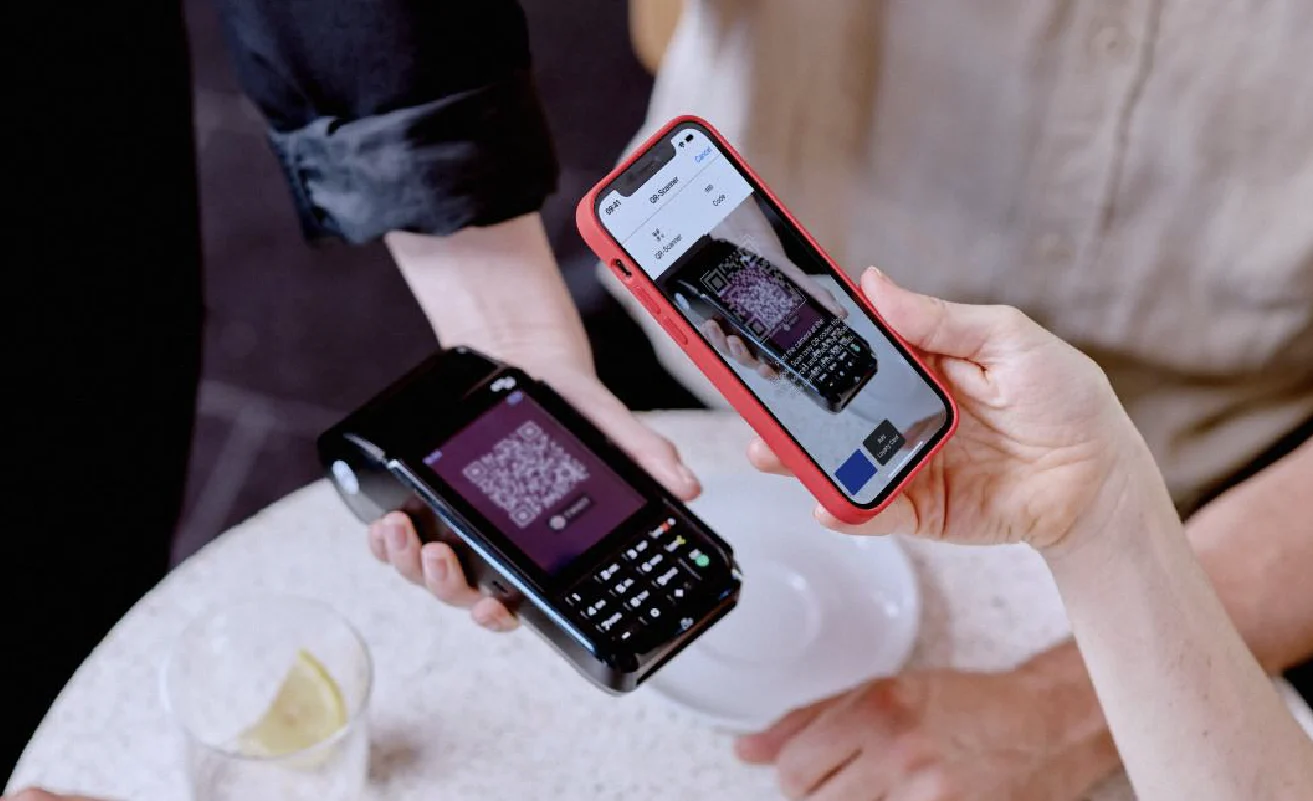 Eine Hand hält ein Handy und scannt damit einen TWINT QR Code auf einem Zahlungsterminal