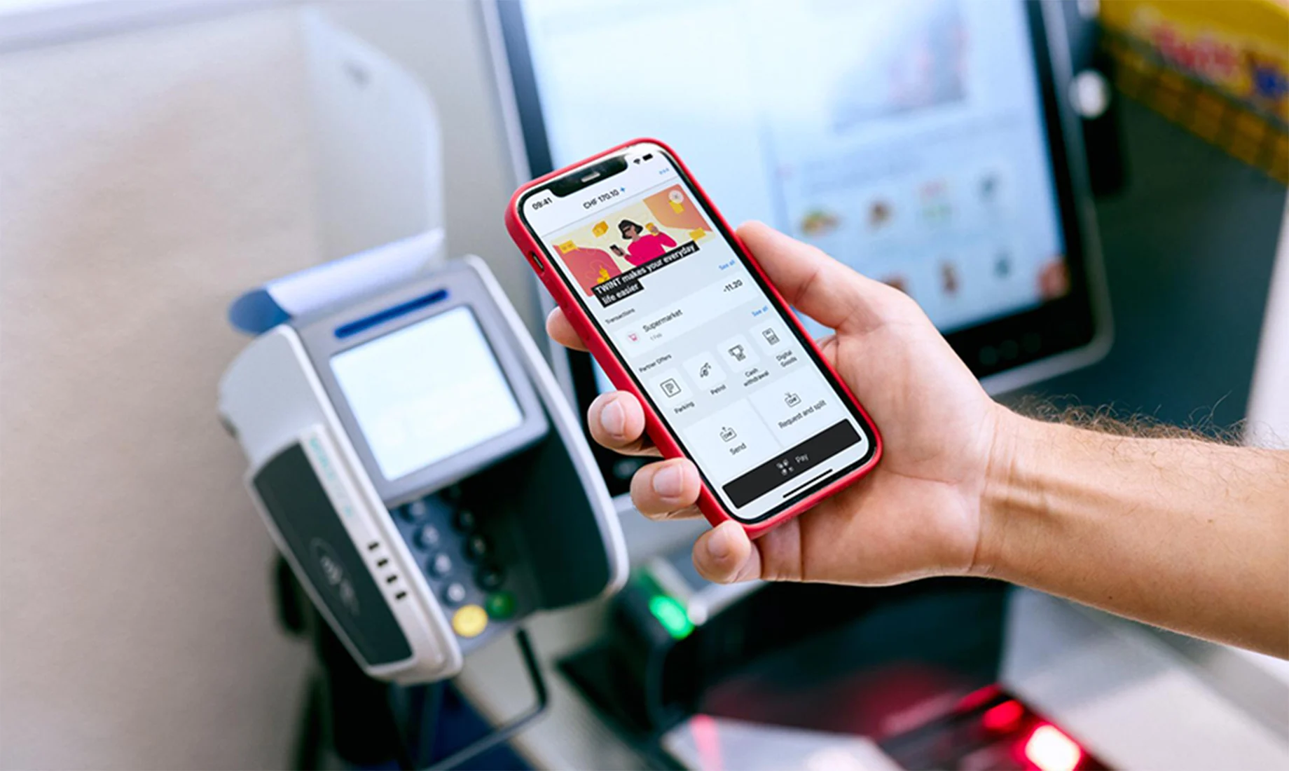 Eine Hand hält ein Handy für die Bezahlung an einem Zahlterminal an der Kasse
